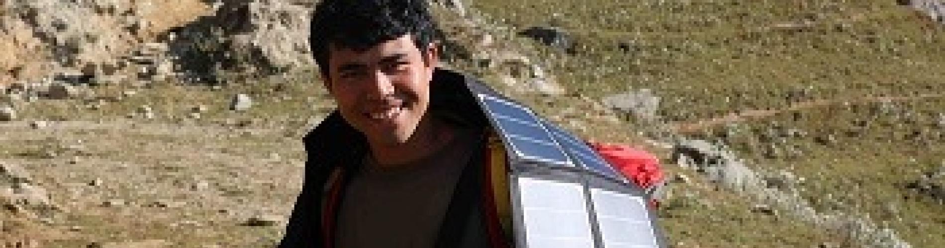Man carrying a large solar panel on a hillside under sunlight.