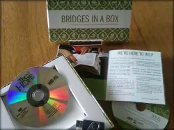 Box set labeled "BRIDGES IN A BOX" with a CD, booklet, and USB drive on a wooden table.