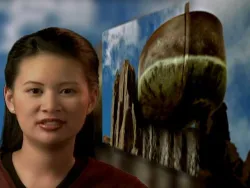 Woman smiling in front of a blurred image of an old boat propped on wooden posts.