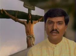 Man in yellow shirt speaking with a crucifixion scene in the background.