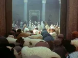 People in robes gather in a courtyard with sheep in the foreground.